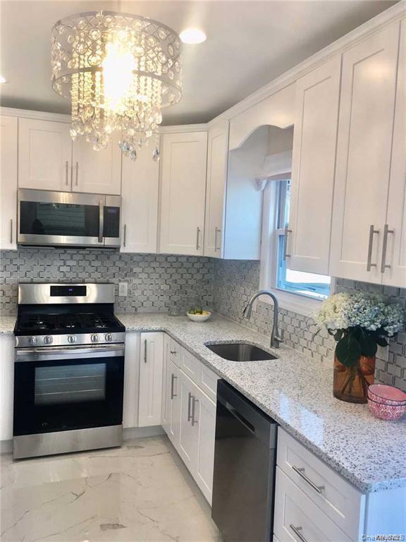 Modern kitchen featuring white shaker cabinetry with brushed nickel hardware, granite countertops, stainless steel appliances, a mosaic tile backsplas