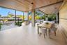 Covered loggia with wood-plank ceiling, recessed lighting, teak dining table, woven outdoor chairs, large-format stone floors, wood accent wall, and o