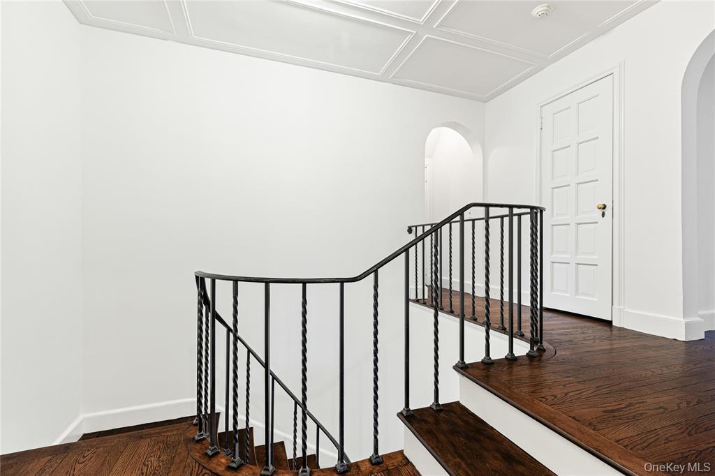 Stairs with arched walkways, wood finished floors, and baseboards