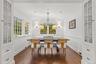 Bright breakfast nook surrounded by windows that fill the space with natural light and peaceful garden views. Classic white wainscoting, warm hardwood