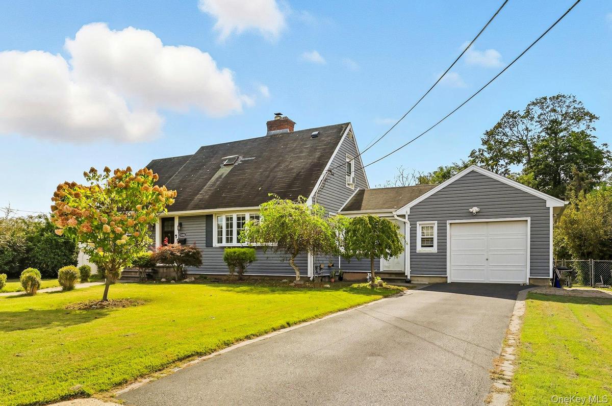 Cape cod home featuring a garage, driveway, a chimney, and a shingled roof
