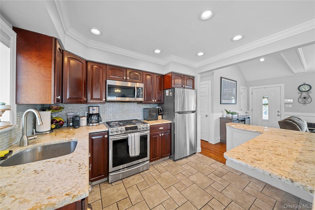 Kitchen featuring stainless steel appliances, light stone counters, recessed lighting, decorative backsplash, and dark wood finish cabinets