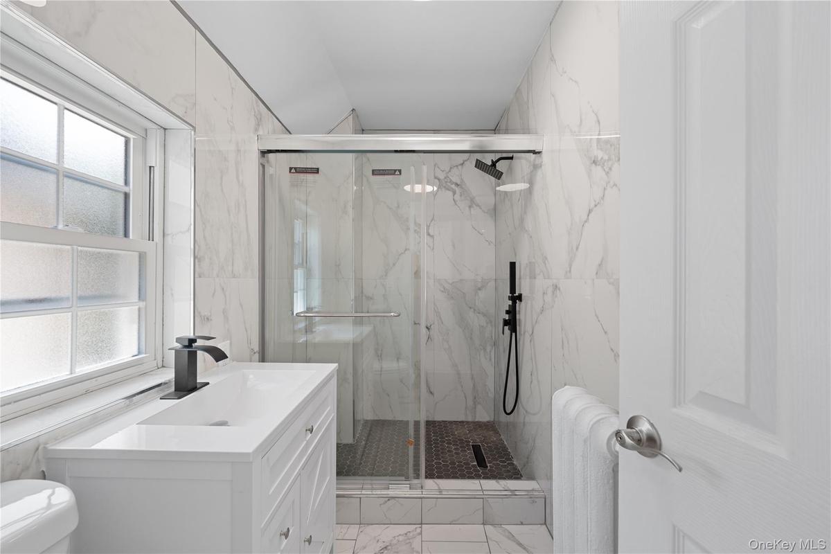 white vanity with integrated rectangular sink and matte black faucet, glass-enclosed shower, matte black shower fixtures, and white marble-look wall t
