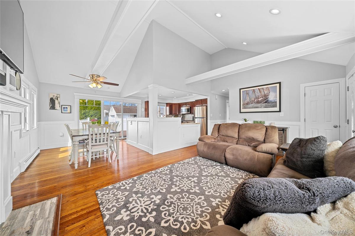 Living room featuring a decorative wall, wainscoting, vaulted ceiling, light wood-style flooring, and baseboard heating