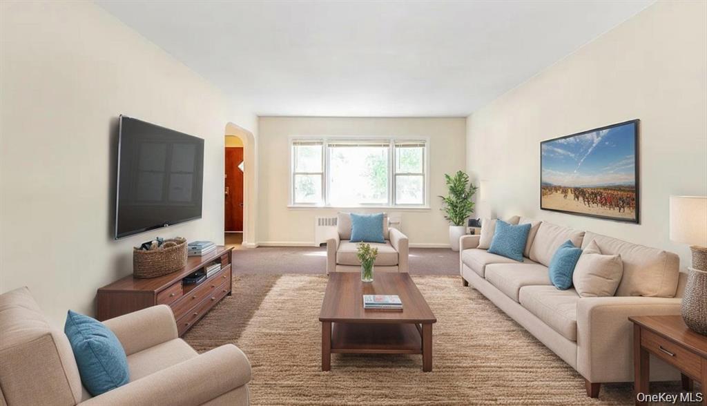 Living area featuring carpet flooring, arched walkways, and radiator