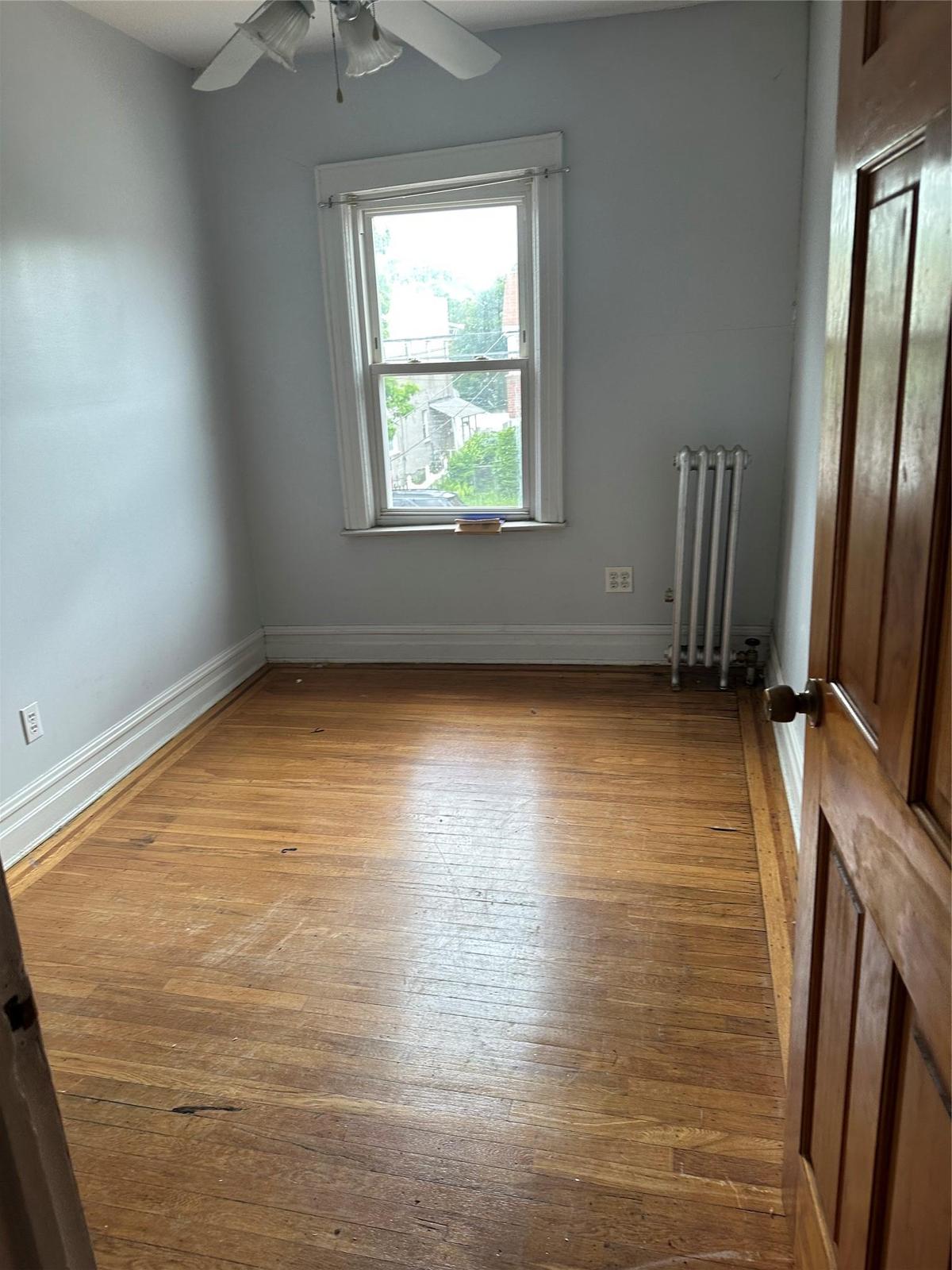 Spare room featuring radiator heating unit, ceiling fan, and wood finished floors
