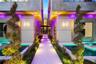 Resort-style entry corridor with dual reflecting pools, spiral topiaries, wood-paneled ceiling, recessed lighting, and illuminated pathway leading to