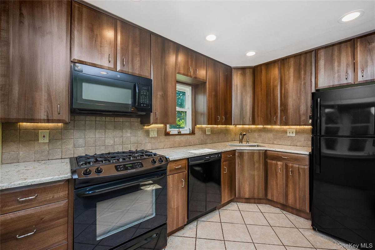 Kitchen featuring wood-finish cabinetry, light-toned countertop, tile backsplash, and black appliances