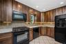 Kitchen featuring wood-finish cabinetry, light-toned countertop, tile backsplash, and black appliances