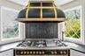 Professional-grade range with a custom black and brass vent hood, ornate cast-iron backsplash, and pot filler