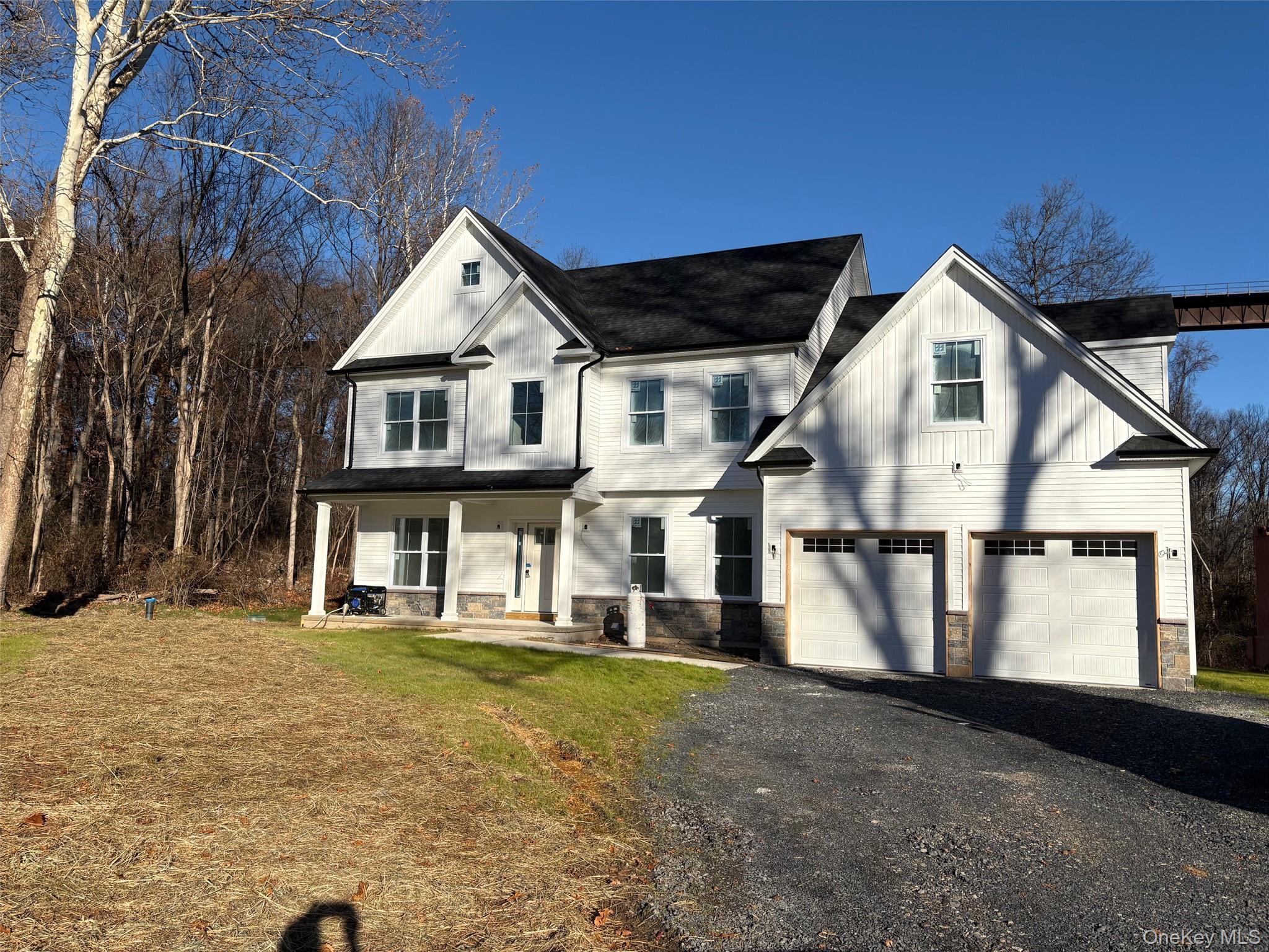 Actual house that is for sale. Modern farmhouse style home featuring stone siding, covered porch, asphalt driveway, a front lawn, and an attached gara
