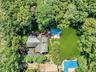 Aerial view of this home's expansive outdoor living space featuring a resort-style pool with surrounding lounge seating, manicured lawn, mature tree-l