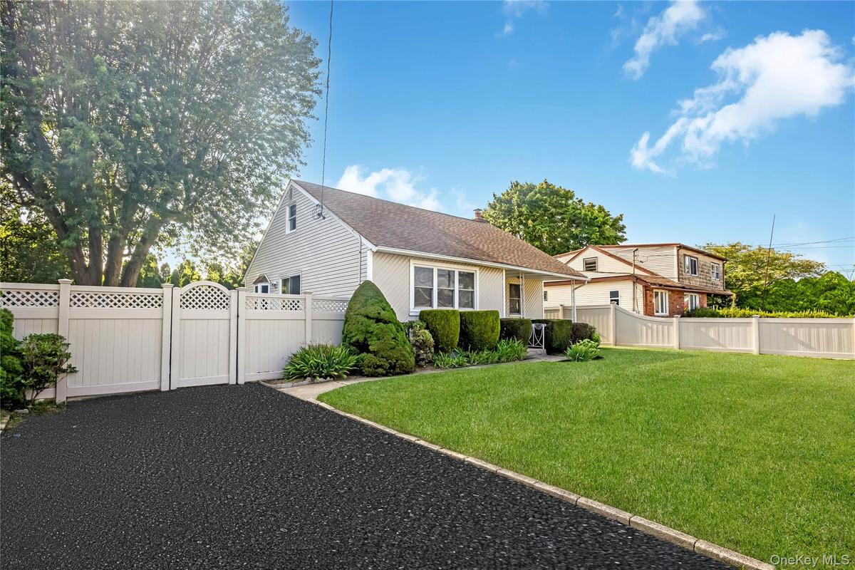 Paved driveway with white lattice-top fencing and gate, mature landscaping, and a manicured lawn