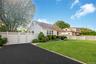 Paved driveway with white lattice-top fencing and gate, mature landscaping, and a manicured lawn