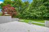 Expansive outdoor deck space featuring painted wood decking, built-in benches, and a planter, with a backdrop of mature trees and a manicured lawn