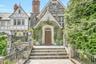 Charming stone entry with classic Tudor detailing, highlighted by an arched wooden door, climbing ivy, and decorative windows. The inviting front step