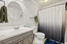 Bathroom featuring a vanity with a white countertop and a gray wood-finish cabinet, a round wall-mounted mirror, and a full shower with a tub