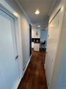 Hallway featuring rich wood-finish flooring, white painted doors, recessed ceiling lighting, and clean white walls with simple trim detailing
