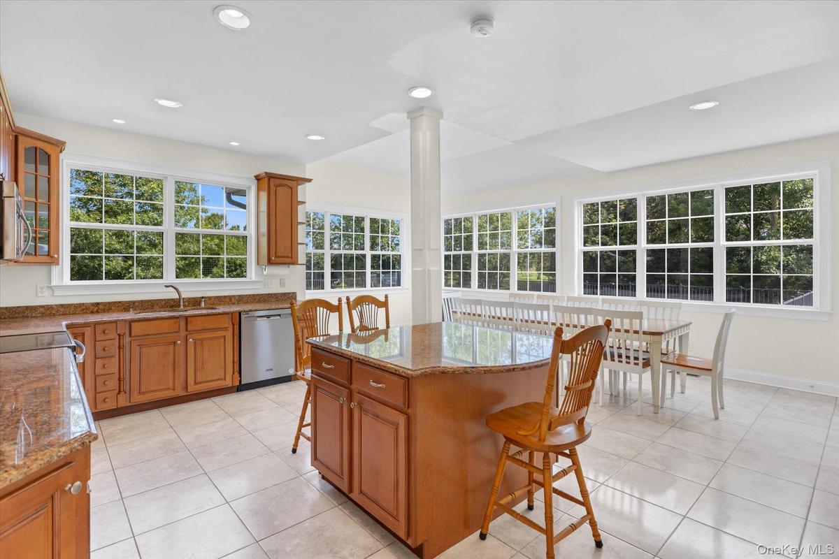 Open-concept kitchen with wood cabinetry, granite countertops, stainless steel dishwasher, a center island, and tile flooring