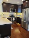 Kitchen with stainless steel appliances, light stone countertops, dark wood finished floors, tasteful backsplash, and dark brown cabinets