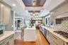Gourmet kitchen with a waterfall edge island, recessed lighting, coffered ceiling detail, gas range, and geometric tile backsplash