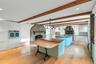 Expansive kitchen featuring exposed wood beams, light wood-finish flooring, a stone fireplace, white cabinetry, and two cherry wood kitchen islands