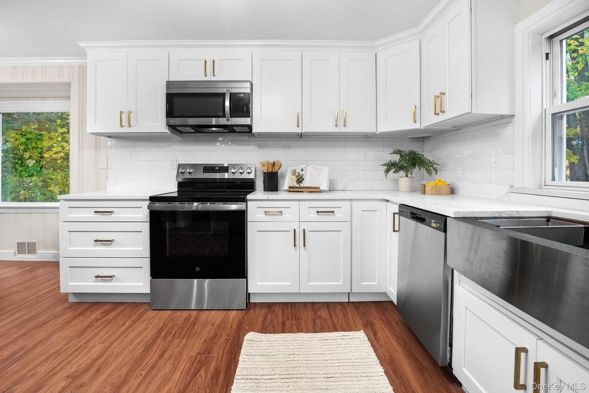 Newly renovated kitchen featuring stainless steel appliances, quartz countertops, and elegant white shaker cabinetry accented with brushed gold hardwa