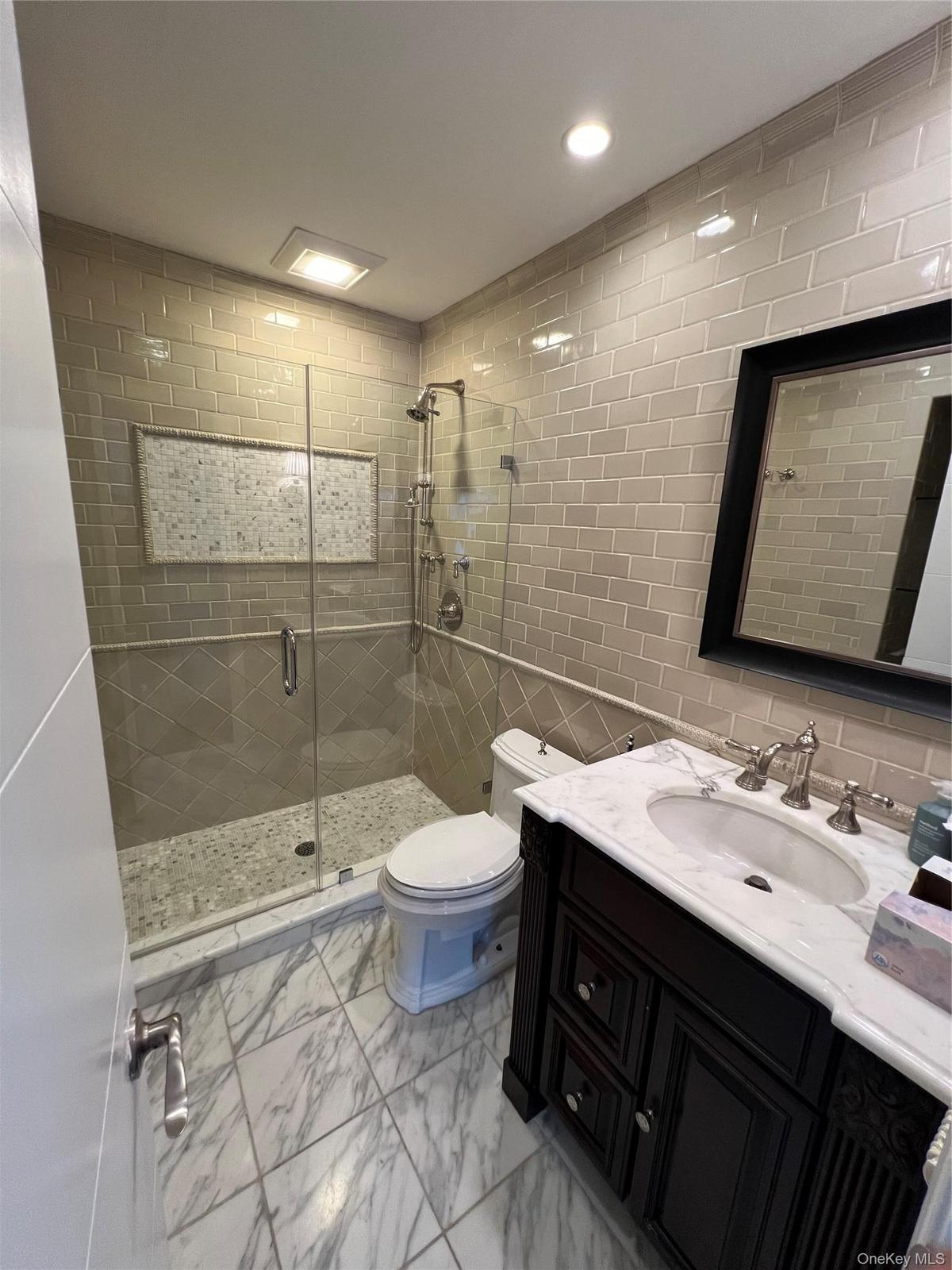Spa-inspired primary bathroom featuring a frameless glass-enclosed walk-in shower with subway tile surround and pebble stone flooring, dual vanity wit