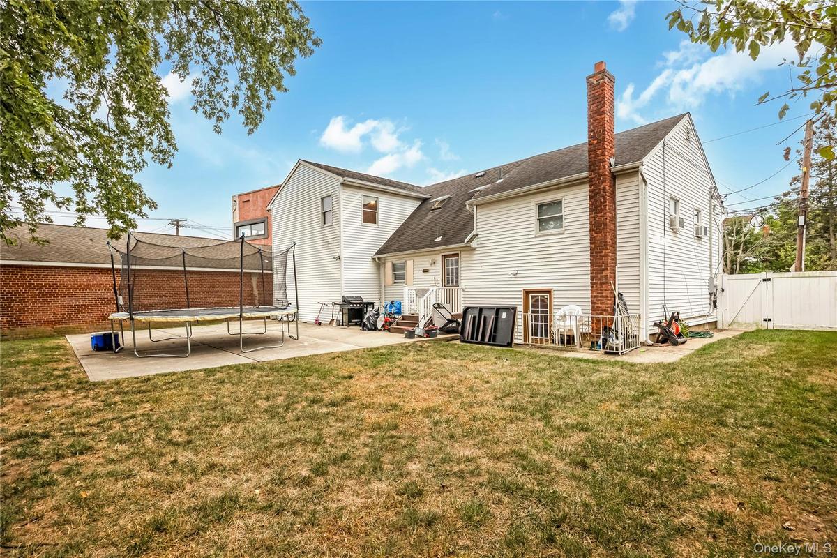 Rear view of property featuring a patio, a gate, a trampoline, a chimney, and a shingled roof