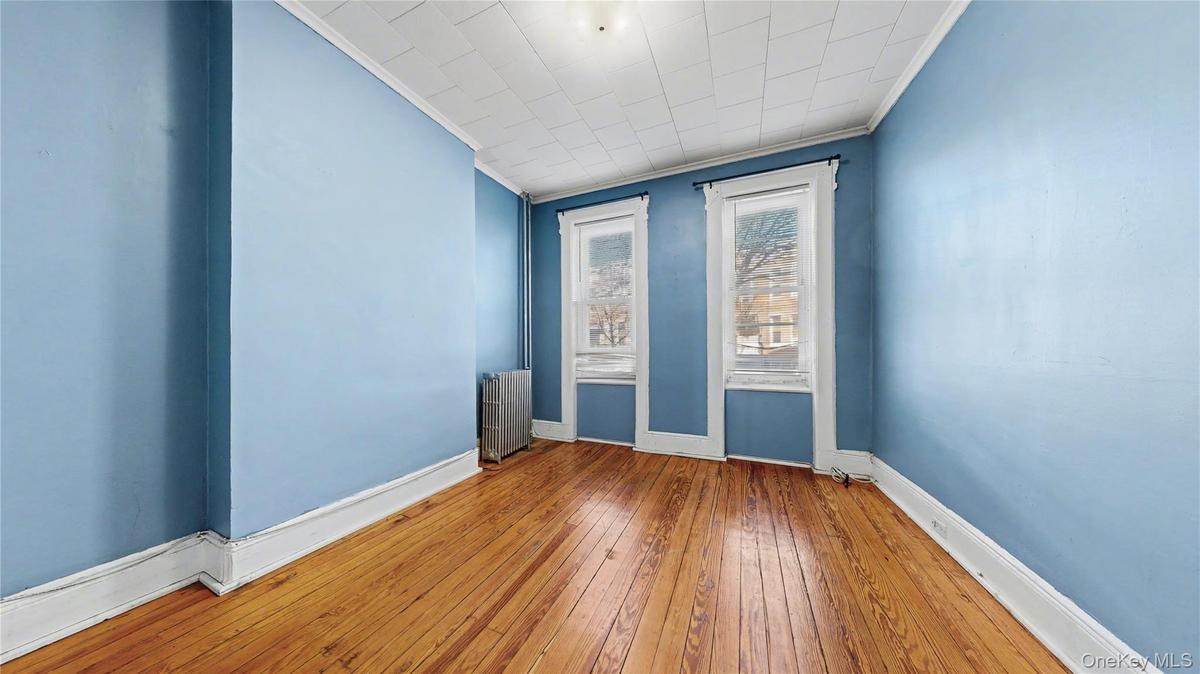 Spare room with ornamental molding, radiator heating unit, and wood-type flooring