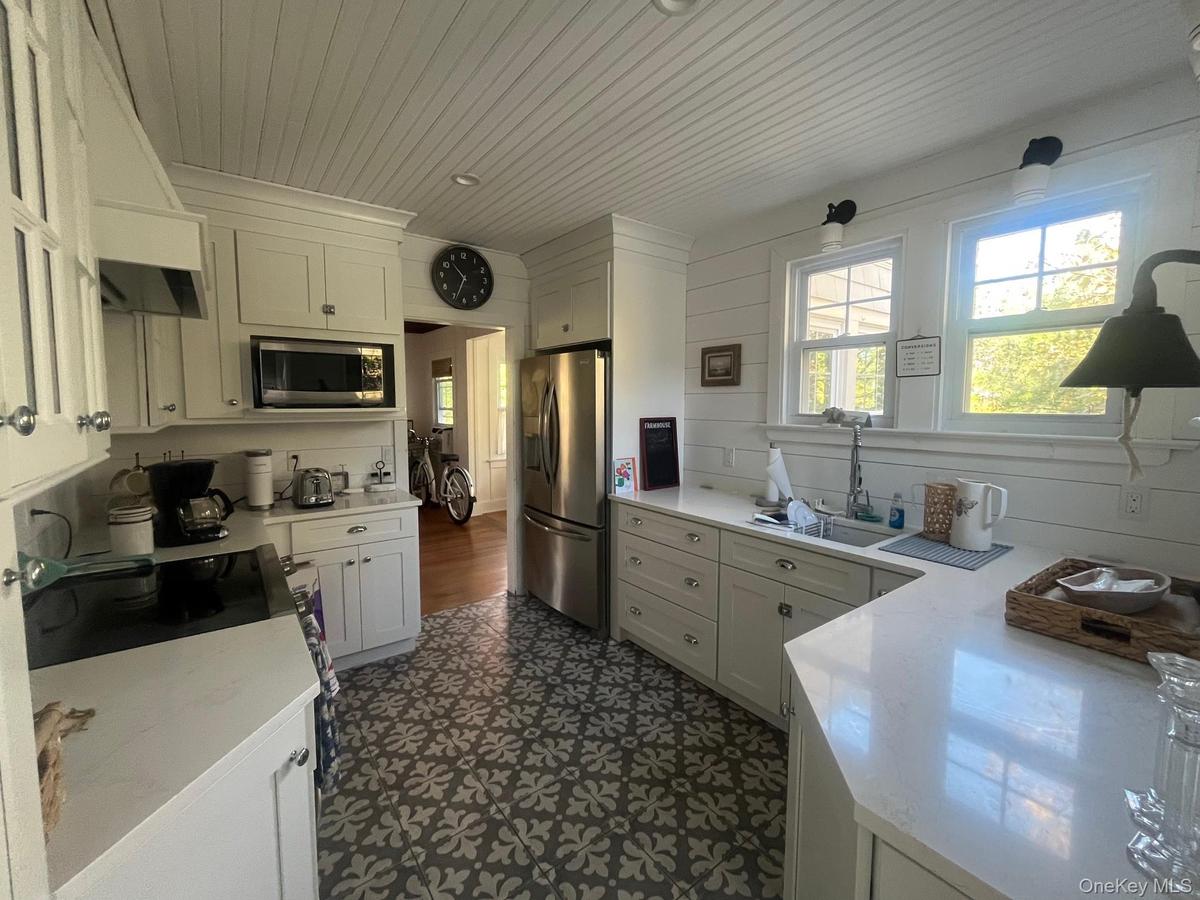 Kitchen with white cabinetry, appliances with stainless steel finishes, premium range hood, light stone counters, and wood ceiling