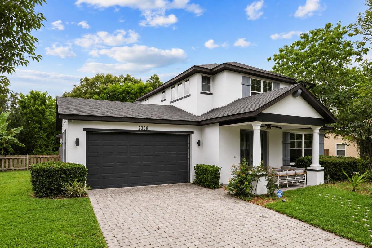 Attractive front exterior showcasing modern architecture,a paver driveway, covered front porch, and attached two-car garage.