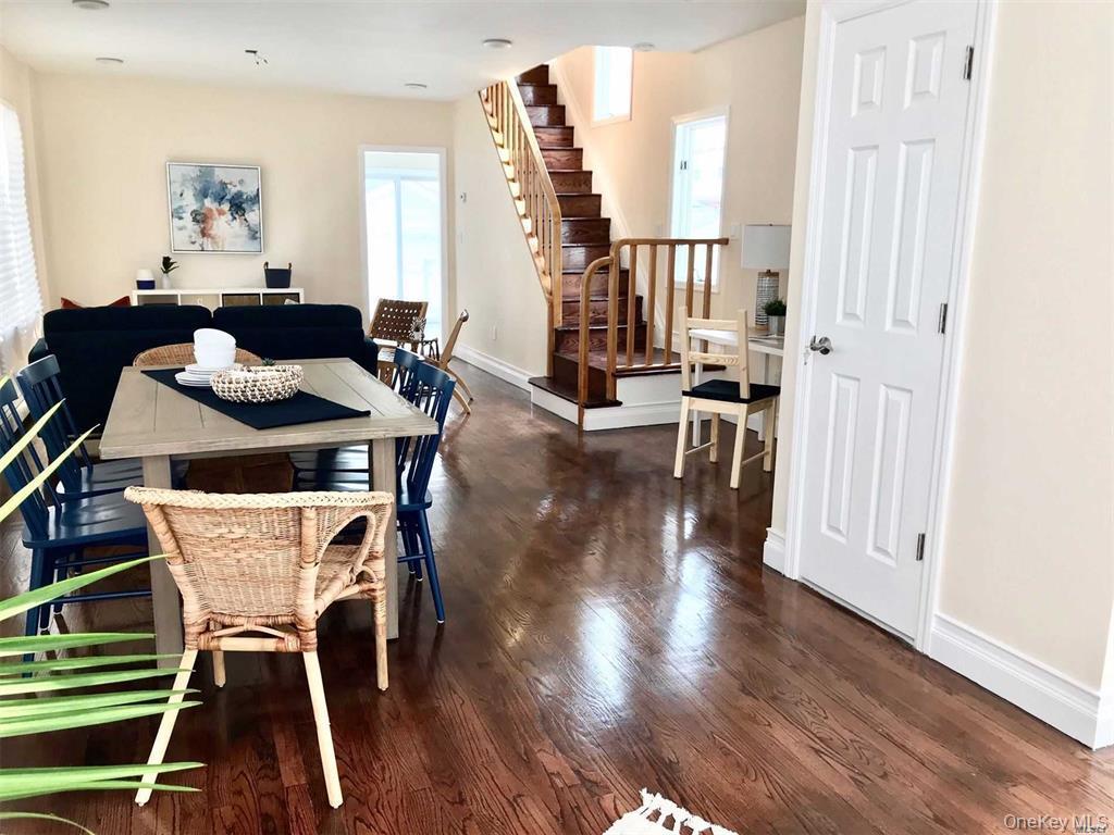 Open-concept living area featuring rich wood-finish flooring, a dining table with seating for multiple guests, and a striking wooden staircase with me