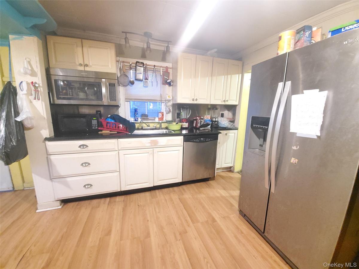 Kitchen featuring appliances with stainless steel finishes, ornamental molding, light wood-type flooring, dark countertops, and white cabinetry