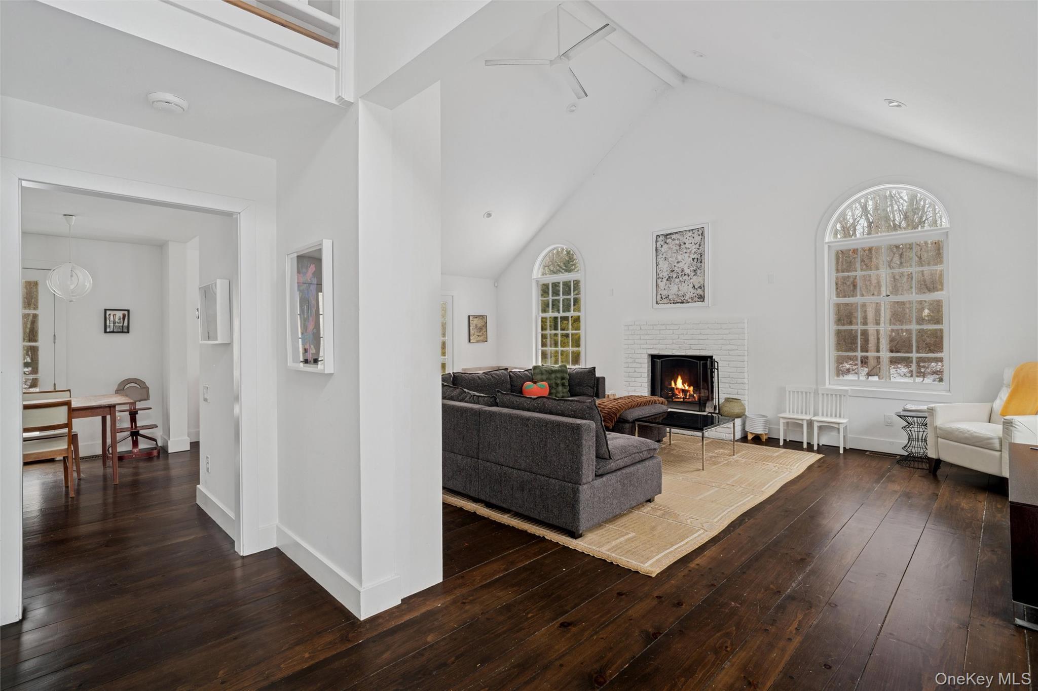 Living area with dark wood-type flooring, high vaulted ceiling, beamed ceiling, a fireplace, and a ceiling fan