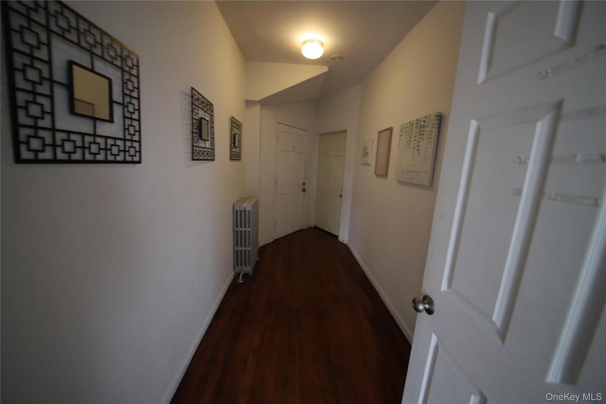 Corridor featuring baseboards, dark wood-style flooring, and radiator heating unit