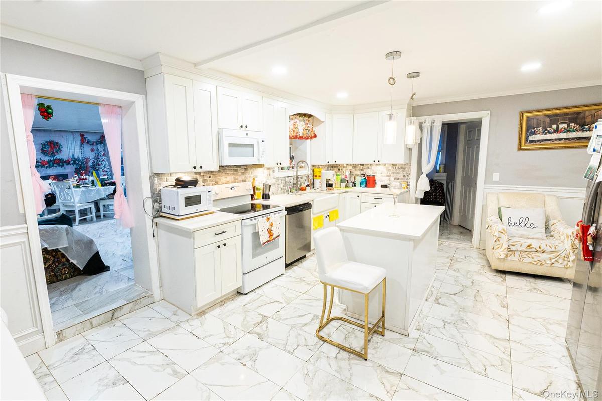 Kitchen featuring a wainscoted wall, crown molding, white appliances, white cabinetry, and light marble finish flooring