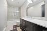 Modern bathroom featuring a dark wood-finish vanity with a white countertop and undermount sink, a large arched mirror, and a tub/shower combination w