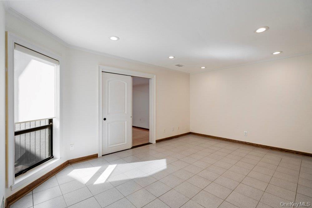 Bright room featuring light-toned tile flooring, recessed ceiling lighting, and a window with a roller shade