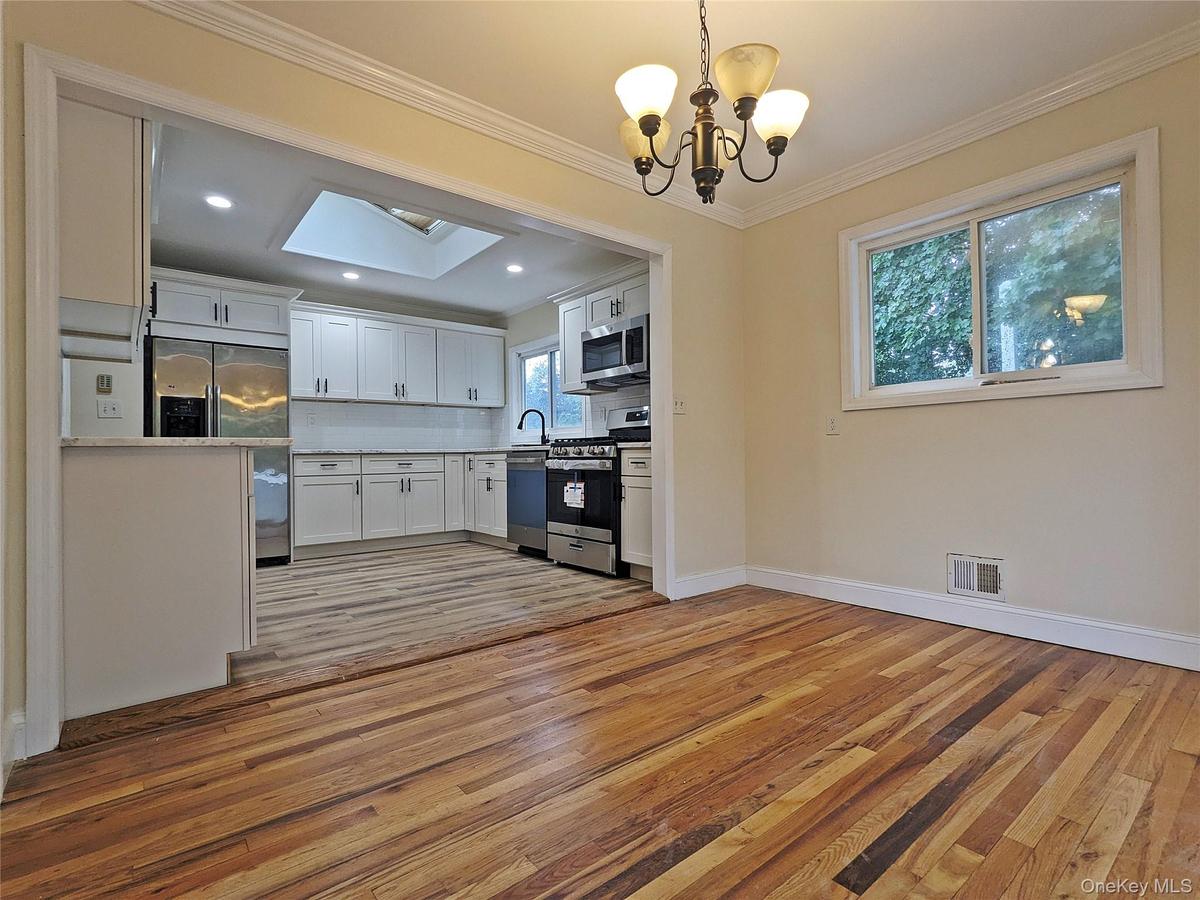 Open-concept dining area with wood-finish flooring, crown molding, and a chandelier, opening to a kitchen featuring white cabinetry, a skylight, and s