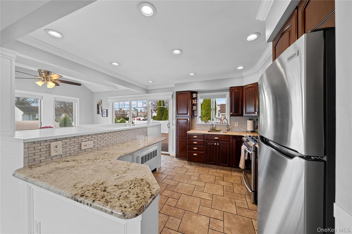Kitchen featuring stainless steel appliances, decorative backsplash, light stone finish flooring, recessed lighting, and ornamental molding