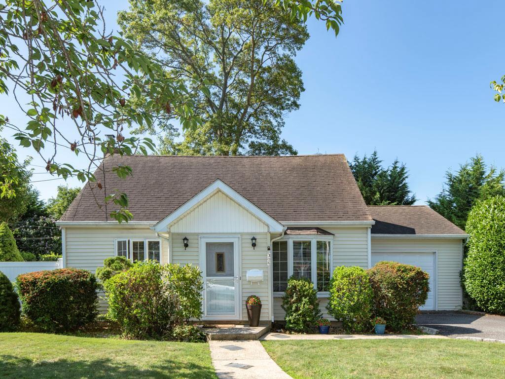 View of front of house with an attached garage, roof with shingles, a front yard, and driveway
