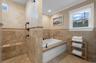 Bathroom with tile walls, healthy amount of natural light, a wainscoted wall, a garden tub, and crown molding