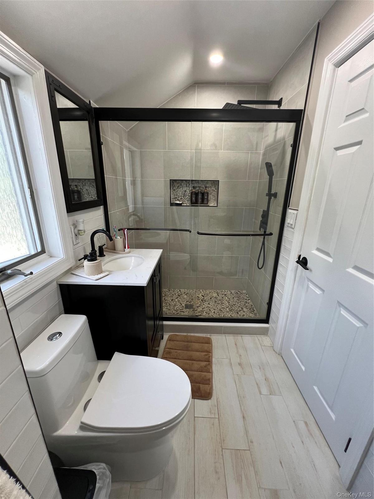 Modern bathroom featuring a glass-enclosed shower with pebble-finish flooring, a contemporary vanity with a white countertop and rectangular sink, and