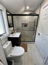 Modern bathroom featuring a glass-enclosed shower with pebble-finish flooring, a contemporary vanity with a white countertop and rectangular sink, and