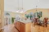Kitchen with light stone counters, pendant lighting, light wood-style flooring, a kitchen island with sink, and a chandelier