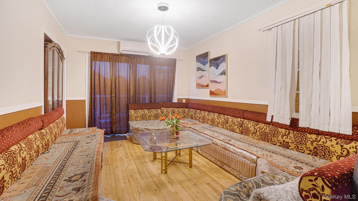 Living area featuring hardwood / wood-style flooring, an inviting chandelier, ornamental molding, and a wall mounted air conditioner