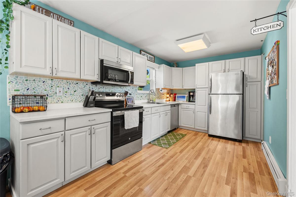 Full kitchen featuring white cabinetry, light-toned countertops, a mosaic tile backsplash, stainless steel appliances, and wood-finish flooring
