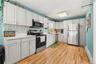 Full kitchen featuring white cabinetry, light-toned countertops, a mosaic tile backsplash, stainless steel appliances, and wood-finish flooring