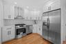 Kitchen featuring stainless steel appliances, white cabinets, wall chimney range hood, light wood finished floors, and recessed lighting